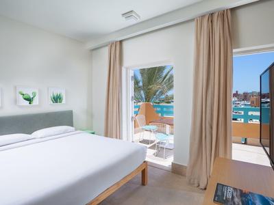 Helles Schlafzimmer mit großem Bett, weißen Wänden, Vorhängen und Blick auf Balkon und Meer.