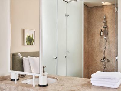 Modernes Badezimmer mit Glasdusche, verchromtem Duschkopf und weißen Handtüchern auf Marmorablage.