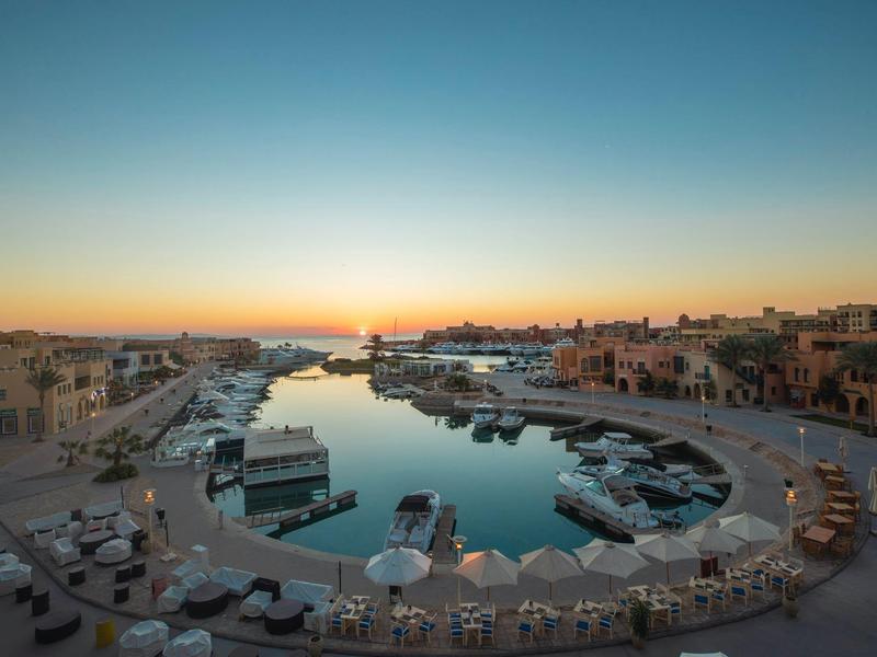 Hafen mit Booten und Restaurants bei Sonnenuntergang, ruhiges Wasser und klarer Himmel.