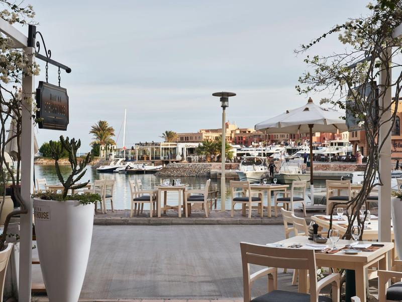 Blick auf eine Marina mit Booten, umgeben von Stühlen, Tischen und Pflanzen auf einer Terrasse.