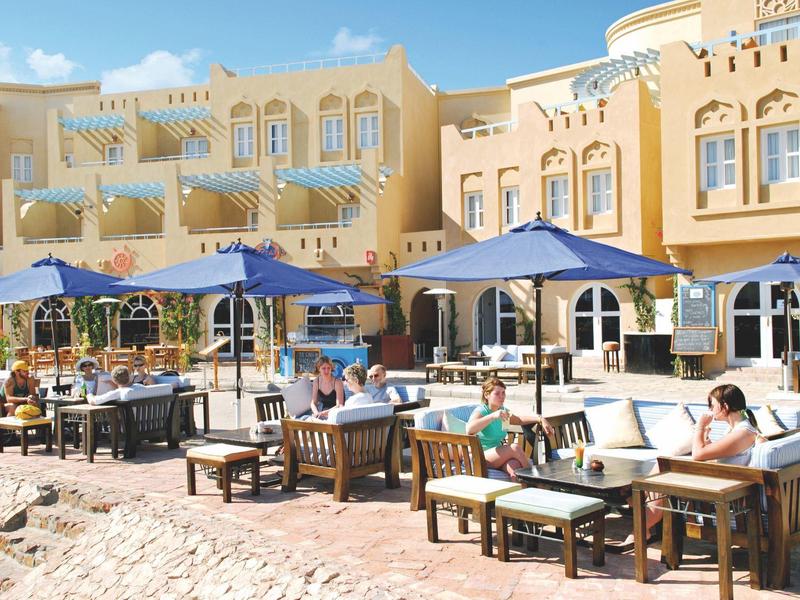 Außenbereich eines Cafés mit Sitzmöbeln, Sonnenschirmen und Menschen, helles sonniges Wetter.