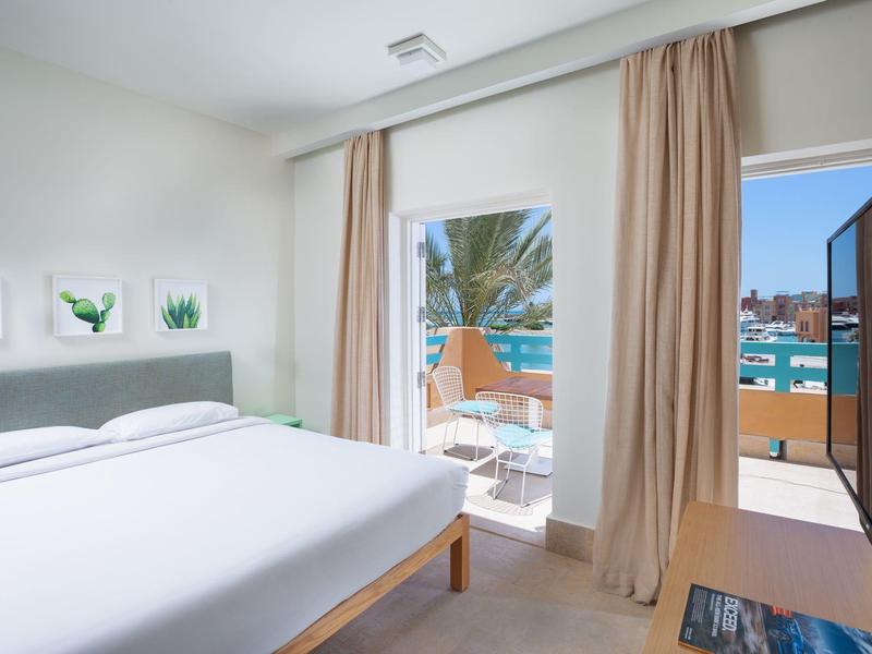 Helles Schlafzimmer mit großem Bett, weißen Wänden, Vorhängen und Blick auf Balkon und Meer.