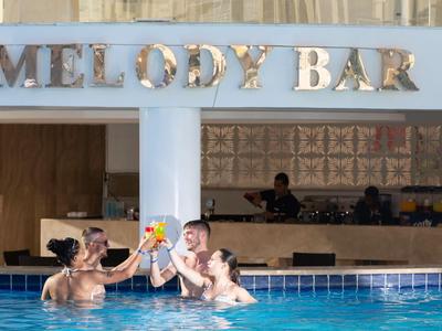 Drei Personen genießen Getränke im Schwimmbad neben der Melody Bar.