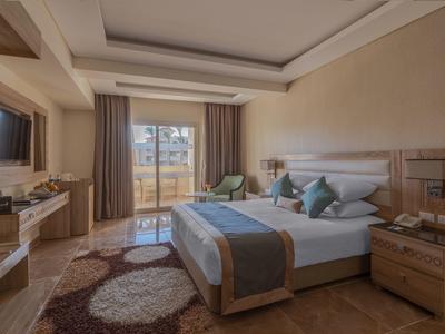 Modernes Schlafzimmer mit großem Bett, Holzmöbeln, Teppich und Balkon mit Glasfront.