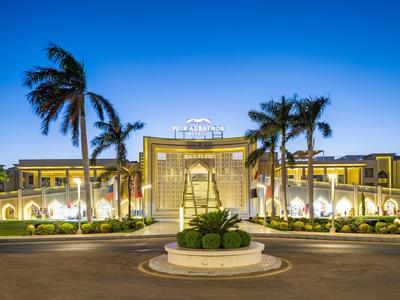Symmetrisches, modernes Gebäude mit Palmen und beleuchteter Fassade bei Dämmerung.