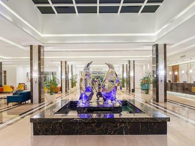 Große helle Hotellobby mit Marmorbrunnen, blauen Skulpturen und modernen Sitzgruppen.