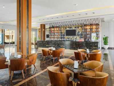 Moderne Bar mit runden Holztischen, braunen Lederstühlen, schwarzer Theke und hellem Marmorboden.