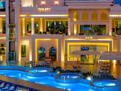 Beleuchtetes Hotel mit modernem Poolbereich und mehreren Ebenen bei Nacht.