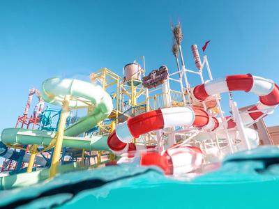Bunte Wasserrutschen in einem Wasserpark unter klarem blauem Himmel, Wasser im Vordergrund.