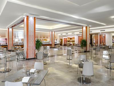 Ampia sala da pranzo moderna con tavoli rotondi, sedie, pavimento chiaro e colonne decorative.