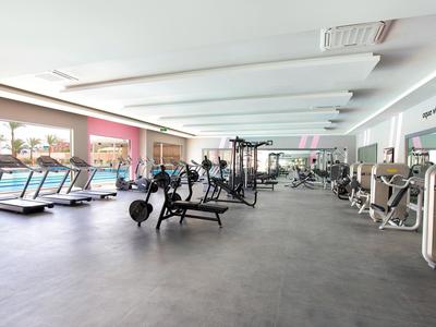 Grande palestra moderna con tapis roulant, attrezzi per il sollevamento pesi e vista sulla piscina esterna.