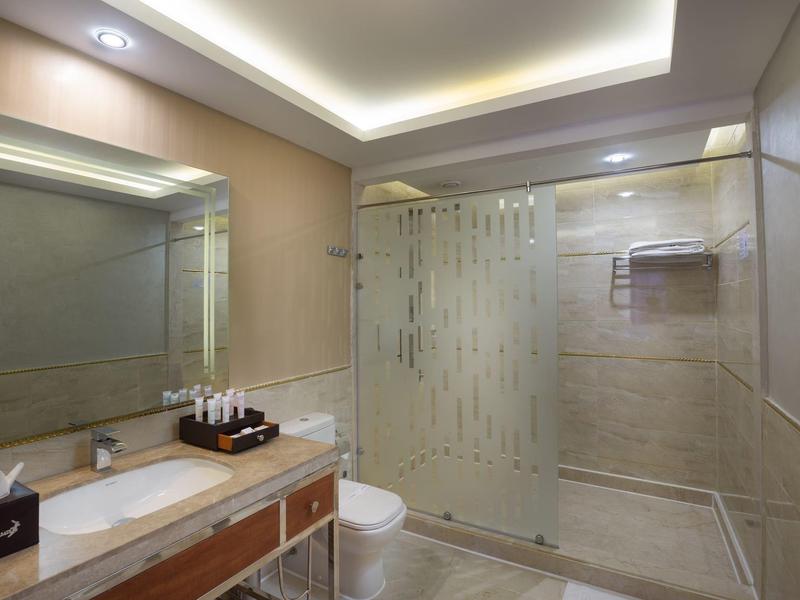 Helle, moderne Badezimmer mit großer Glasdusche, Spiegel, Beleuchtung und Waschbecken mit Ablagefläche.