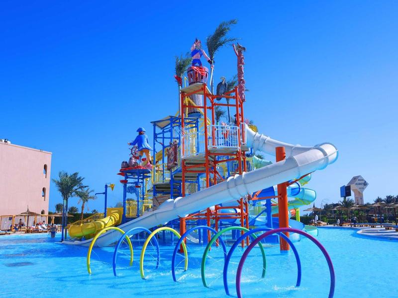 Wasserpark mit bunten Rutschen, blauer Poolfläche und klarem Himmel im Hintergrund.