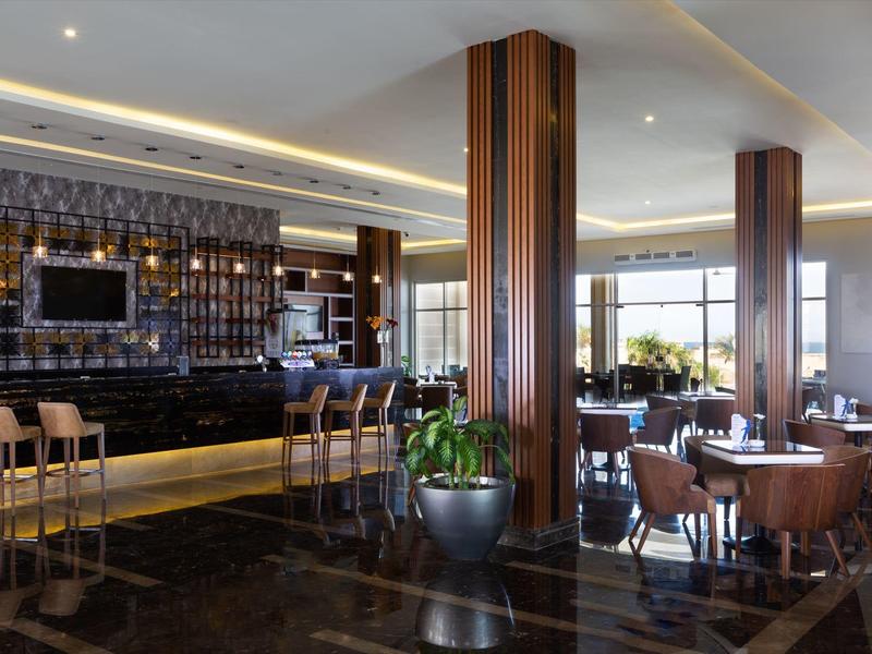 Modernes Restaurant mit Holztischen, Ledersesseln, Holzsäulen und großer Bar mit Barhockern.