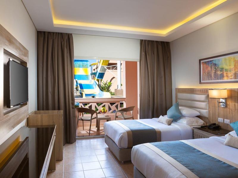 Modern eingerichtetes Hotelzimmer mit zwei Einzelbetten, Balkon und Stadtblick bei Tageslicht.