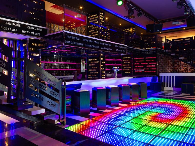 Bunte LED-Tanzfläche mit Bar, Hockern und mehrstöckiger Beleuchtung in modernem Club.