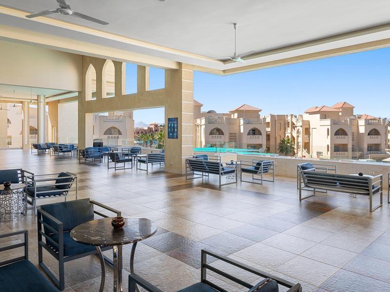 Große Terrasse mit Tischen und Stühlen, Blick auf Pool und beige Gebäude im Sonnenlicht.