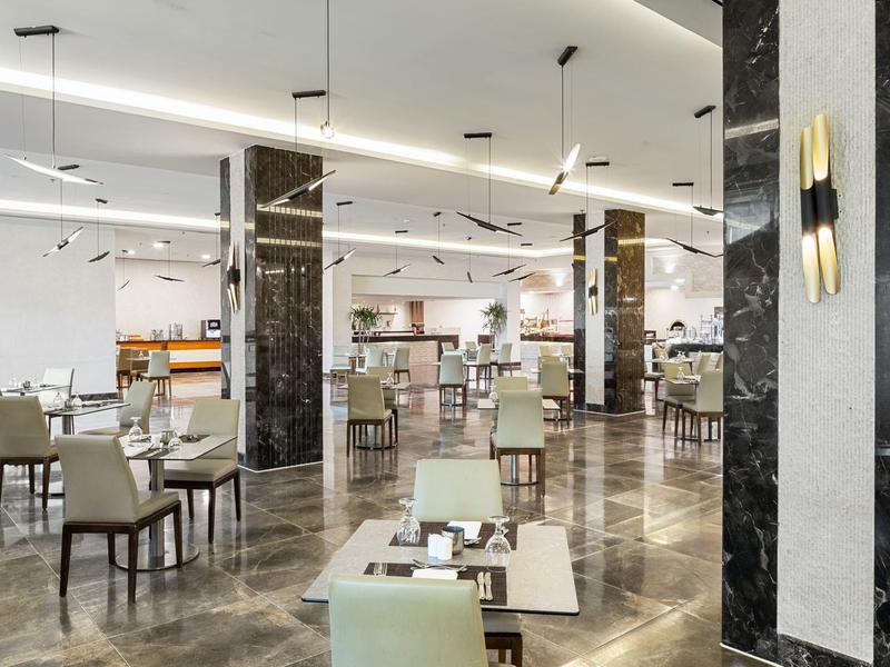 Großer, heller Hotelrestaurantbereich mit modernen Stühlen, Tischen und Marmorboden.