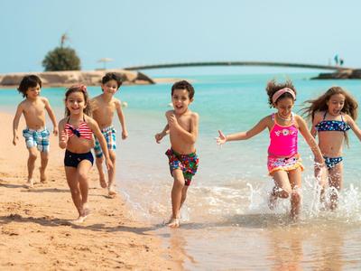 Enfants courant et jouant sur une plage ensoleillée près de l'eau turquoise.