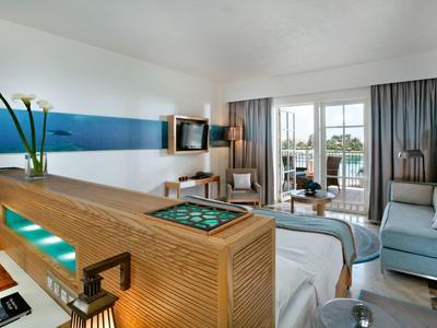 Chambre d'hôtel moderne avec décoration boisée, salle de bain vitrée, terrasse et vue sur la mer.
