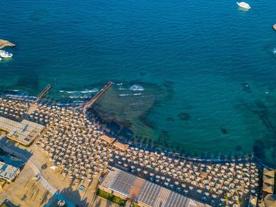 Luchtfoto van een strand met parasols, steigers en helder zeewater.