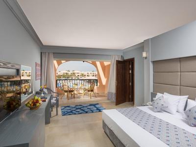 Hell eingerichtetes Hotelzimmer mit Bett, TV und Balkon mit Meerblick.