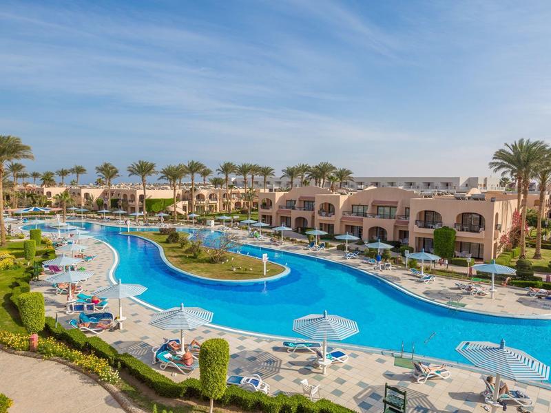 Großer Hotelpool mit Sonnenliegen und Palmen unter blauem Himmel.