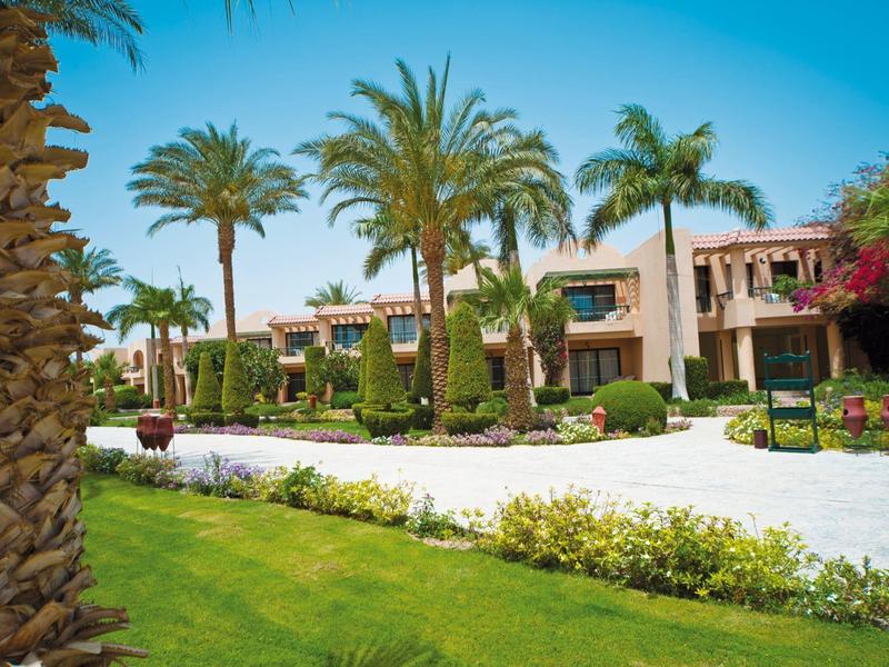Hotelgarten mit Palmen, grünem Rasen und mediterranen Gebäuden unter blauem Himmel