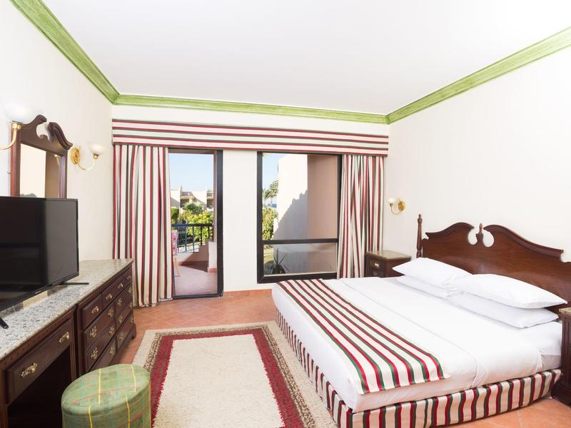 Helles Hotelzimmer mit Doppelbett, TV, Balkon und gestreifter Dekoration