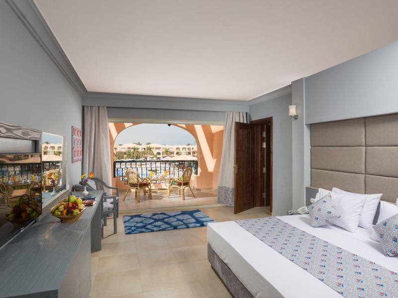 Hell eingerichtetes Hotelzimmer mit Bett, TV und Balkon mit Meerblick.