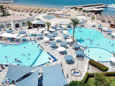 Grande piscina dell'hotel con ombrelloni e lettini vicino al mare in un villaggio turistico.