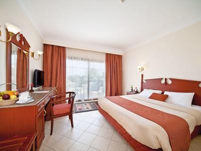 Helles Hotelzimmer mit großem Bett, rot-weißer Einrichtung und Blick durch Panoramaglas.