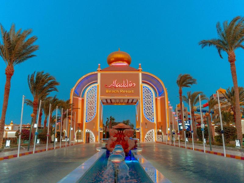 Großer bunter Eingangsbogen mit Palmen und Wasserspielen bei klarem blauem Himmel.