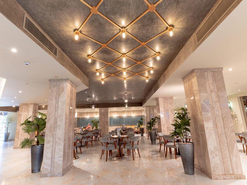 Eleganter Hotelrestaurantbereich mit Marmorboden, Säulen und gedeckten Tischen unter warmem Decklicht.