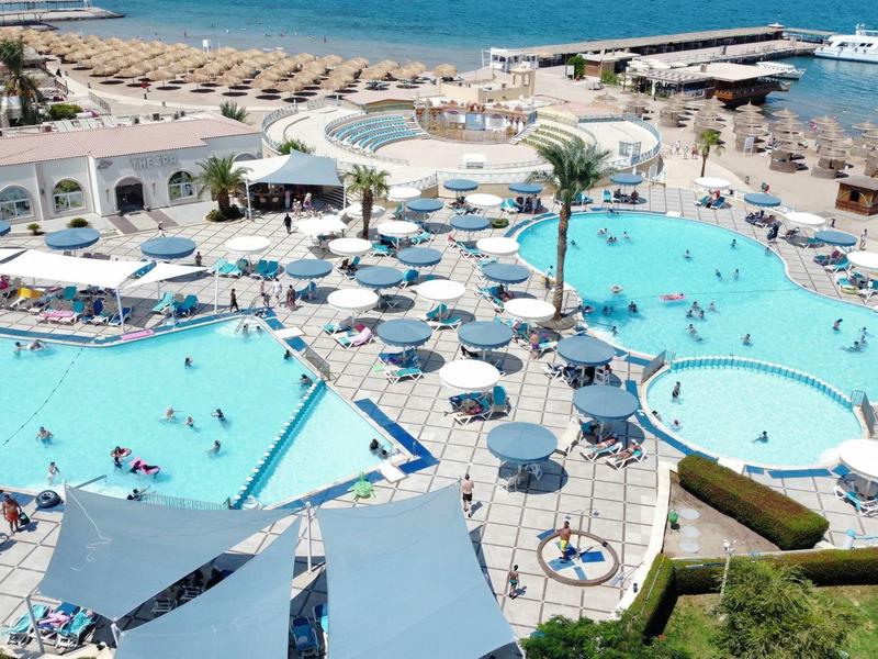 Großer Hotelpool mit Sonnenschirmen, Liegen und Blick auf den Strand und das Meer.