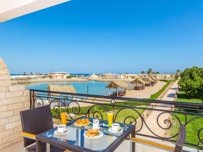Balkon mit Tisch und Frühstück, Blick auf Meer, Sandstrand und blauen Himmel bei sonnigem Wetter.