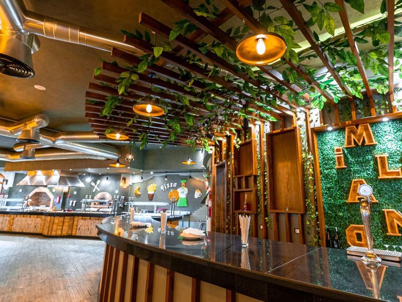 Moderner Barbereich mit grün dekorierter Wand, Holzmöbeln und warmen Deckenlampen.