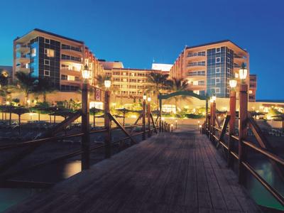 Waterfront hotel at dusk with lights glowing and wooden pier leading to the entrance.