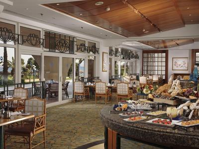 Spacious hotel dining room with wooden ceiling, tables set for meals, and large windows overlooking greenery.