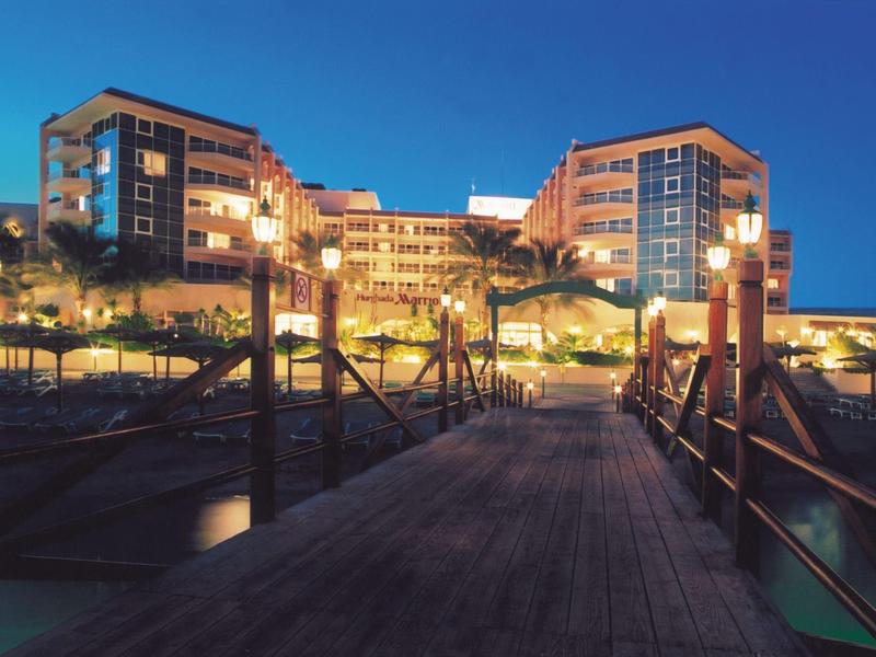 Waterfront hotel at dusk with lights glowing and wooden pier leading to the entrance.