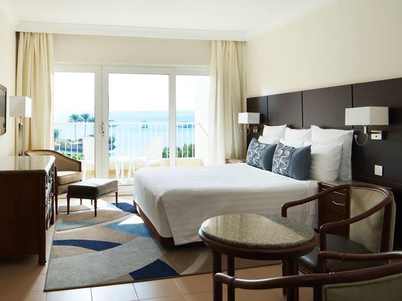 Bright hotel room with king bed, ocean view balcony, and modern furnishings.