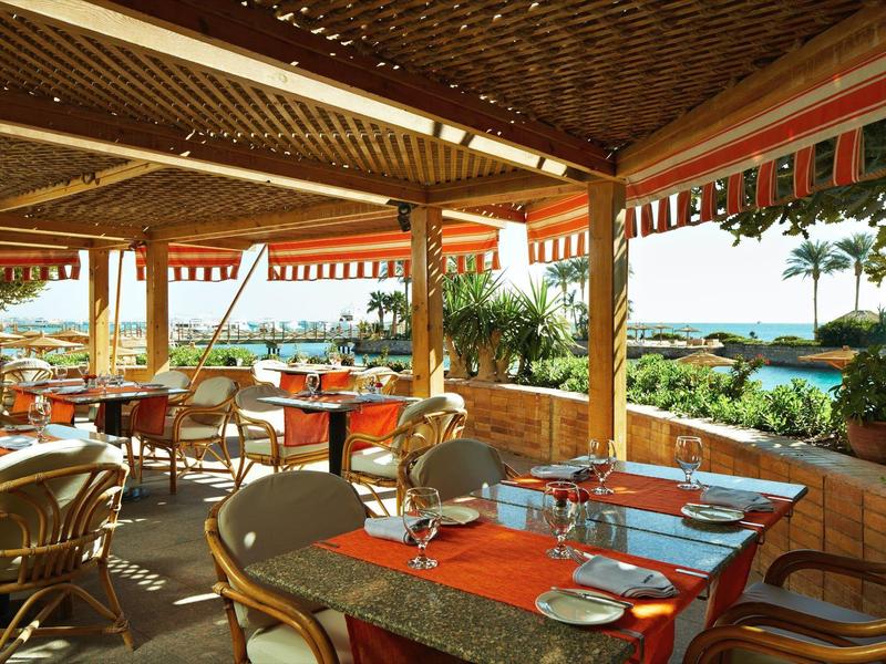 Outdoor restaurant seating with tables set, overlooking a tropical garden and ocean view.