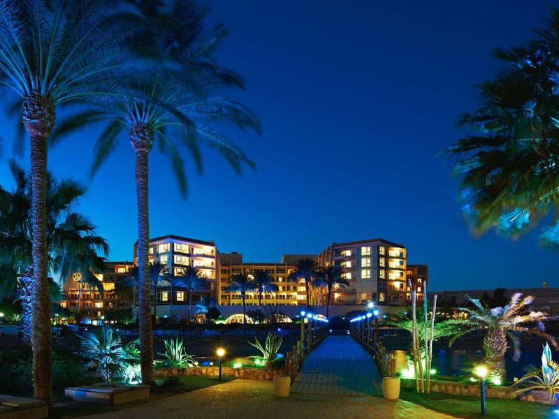 Luxurious hotel lit at night surrounded by palm trees and inviting pools.