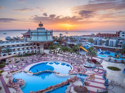 Hotel resort with multiple pools, sun umbrellas, and loungers at sunset by the sea.