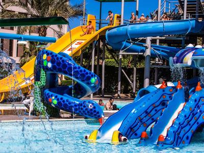 Kinder spielen auf bunten Wasserrutschen in einem Poolbereich eines Hotels bei sonnigem Wetter.