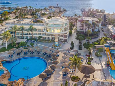 Luxuriöses Resort mit Poolanlagen, Palmen und Ausblick auf das Meer bei sonnigem Wetter.