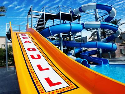 Wasserrutsche mit gelbem Startbereich und blauer Spirale neben Pool unter blauem Himmel.