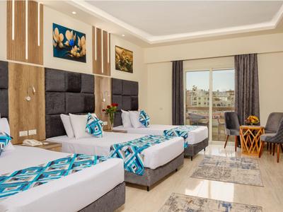 Hell eingerichtetes Hotelzimmer mit drei Betten, Balkon und Sitzbereich mit Tisch und Stühlen.