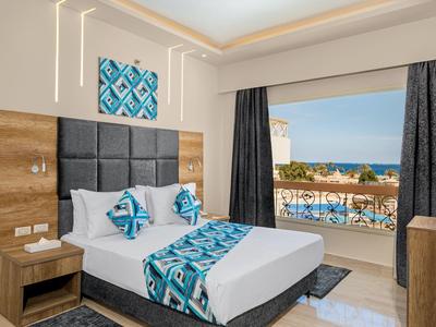 Helles Hotelzimmer mit Doppelbett, blau-weiß gemusterten Textilien und Balkon mit Meerblick.