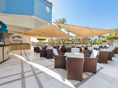 Hotel outdoor area with tables, chairs, and sunshades under clear sky.